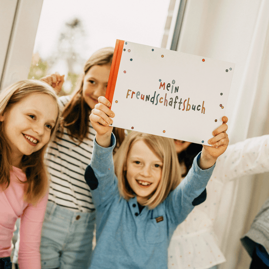Fröhlich lachende Kinder halten Freundebuch Konfetti in die Luft