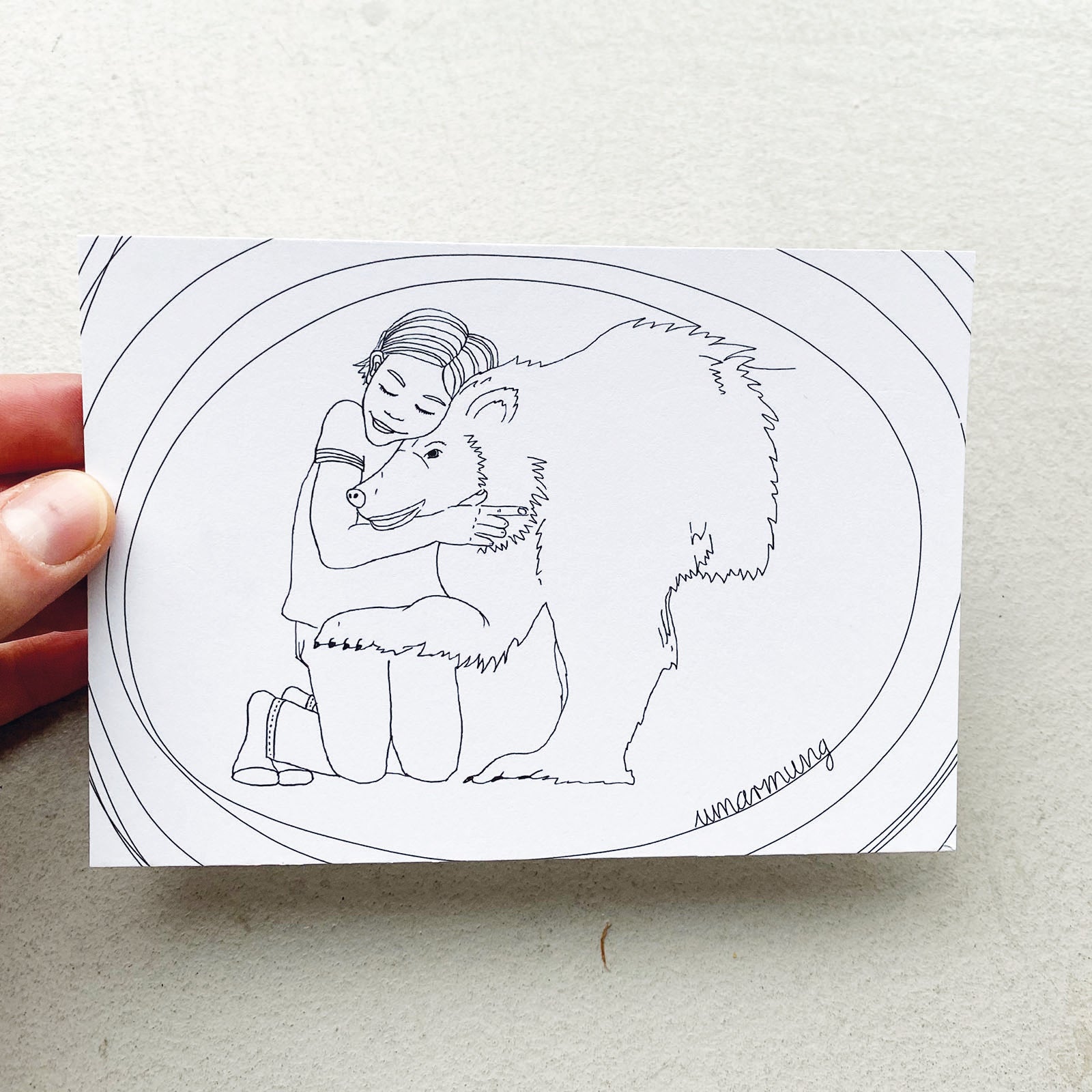 Postkarte mit schwarz weiß handgezeichnetem Motiv, Mädchen umarmt Bär. Schriftzug Umarmung